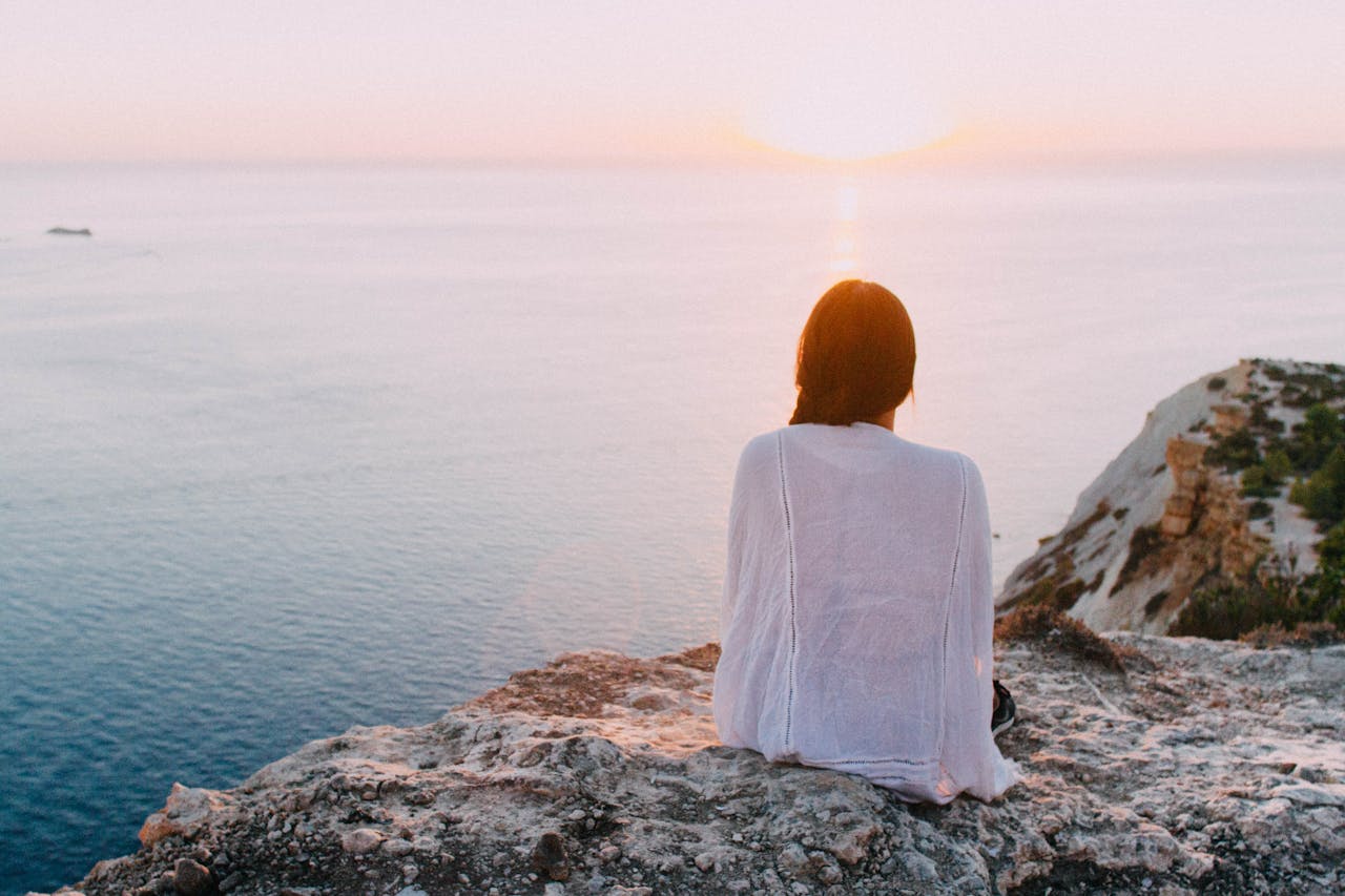 A woman sitting in front of a cliff thinking about her inner child and spirituality.