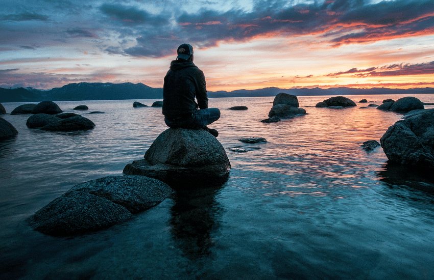 Person sitting on a rock in the water thinking about stress counseling Seattle.